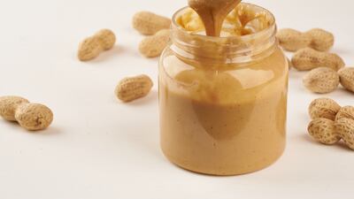 jar of peanut butter and peanuts in a shell on a white table, side view, fresh ground crushed nuts, side view